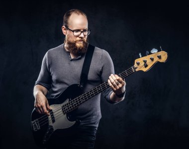 Kızıl saçlı sakallı erkek müzisyen elektro gitar çalmak Gri tişört giymiş gözlük takıyorum. Karanlık dokulu bir arka plan üzerinde izole.
