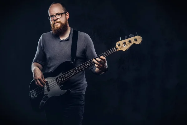 Redhead bearded male musician wearing glasses dressed in a gray t-shirt playing on electric guitar. Isolated on a dark textured background.