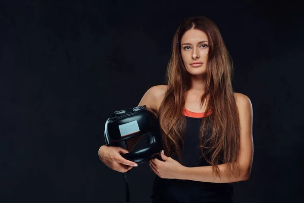 スポーツ ウエアで美しいブルネット女性ボクサーの肖像画は カメラを見て 保護用のヘルメットを保持しています ダーク テクスチャ背景に分離 — ストック写真