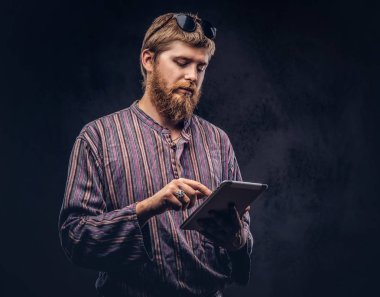 Kızıl saçlı sakallı hippi herif bir tablet bilgisayar kullanarak bir eski moda gömlek giymiş. Karanlık bir arka plan üzerinde izole.