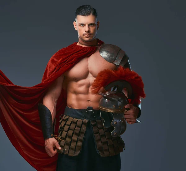 野蛮的古希腊战士 在战斗制服的肌肉强健的身体持有头盔 而站在工作室 在灰色背景上隔离 — 图库照片