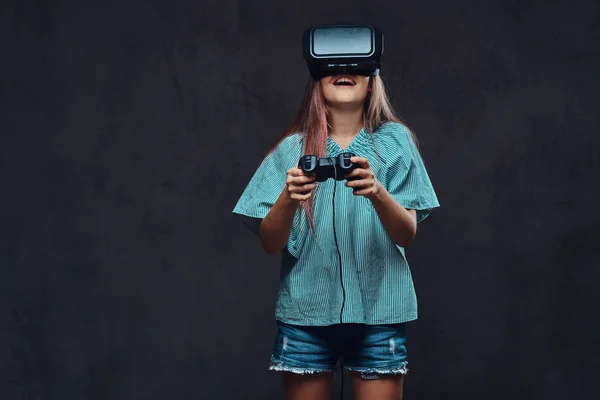 Menina vestida casual jogando o jogo com o joystick e óculos de realidade virtual. Isolado em fundo escuro texturizado . — Fotografia de Stock