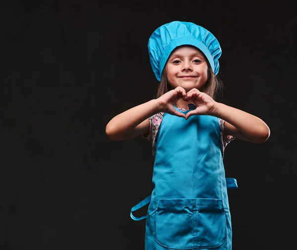 Mavi aşçı üniforma giymiş mutlu küçük kız aşk hareketi gösterir. Karanlık dokulu bir arka plan üzerinde izole. — Stok fotoğraf