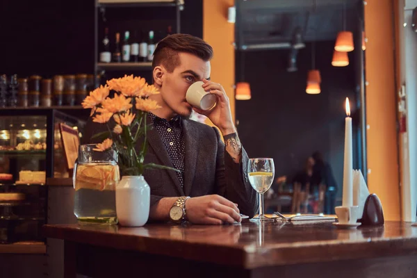 Πορτρέτο του ένας όμορφος άντρας με στιλάτα γένια και μαλλιά, ντυμένοι με ένα μαύρο κοστούμι που κάθεται σε ένα καφέ, ποτά πρωινό καφέ. — Φωτογραφία Αρχείου