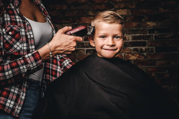 Happy preschooler boy getting haircut. Children hairdresser with trimmer is cutting little boy in the room with loft interior.