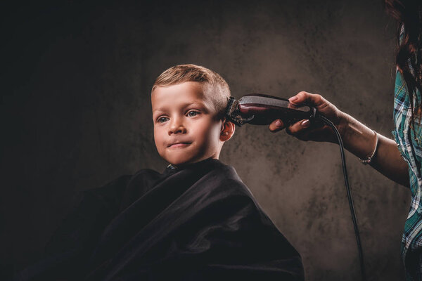 Close-up portrait of a cute preschooler boy getting haircut on a dark background.