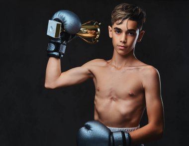 Eldiven giymiş genç gömleksiz boksör şampiyonu Galipleri Kupası tutar. Karanlık bir arka plan üzerinde izole.