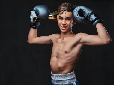 Eldiven giymiş neşeli genç gömleksiz boksör şampiyonu Galipleri Kupası tutar. Karanlık bir arka plan üzerinde izole.