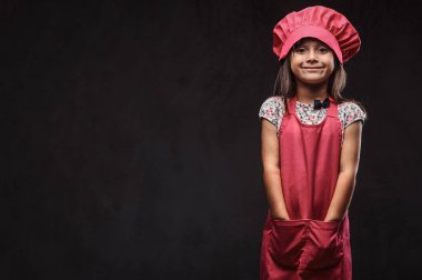 Sevimli küçük kız pembe aşçı üniforma giymiş ceplerinde silah tutar. Karanlık dokulu bir arka plan üzerinde izole.