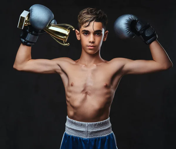 Eldiven giymiş genç gömleksiz boksör şampiyonu Galipleri Kupası tutar. Karanlık bir arka plan üzerinde izole.