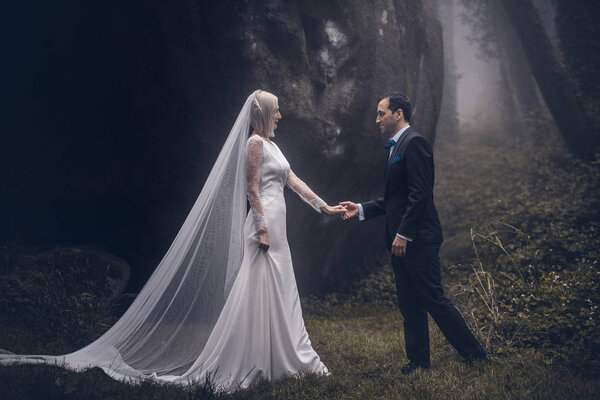 Lovely couple of newlyweds - bride and groom at a beautiful mystery forest with amazing autumn fog.