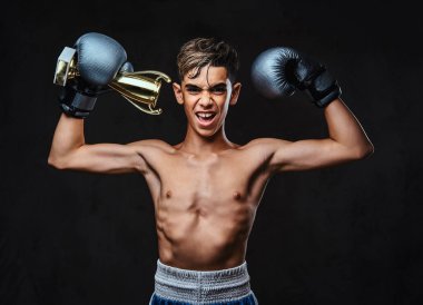 Eldiven giymiş neşeli genç gömleksiz boksör şampiyonu Galipleri Kupası tutar. Karanlık bir arka plan üzerinde izole.