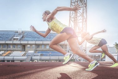 Two female sprinter athletes running on the treadmill race during training in the athletics stadium. clipart