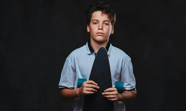 一个穿着白色 T恤衫的年轻溜冰男孩的肖像持有长板 在黑暗背景下被隔离 — 图库照片