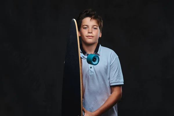 一个穿着白色 T恤衫的年轻溜冰男孩的肖像持有长板 在黑暗背景下被隔离 — 图库照片