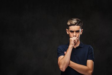 Siyah t-shirt ayakta çapraz kollu yakışıklı dalgın genç adam giymiş. Koyu arka plan üzerinde izole.