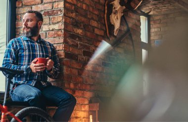 Studio loft iç pencere pervazına üzerinde otururken sabah kahve yakışıklı sakallı hippi erkek mavi Polar gömlek ve pantolon tutar.