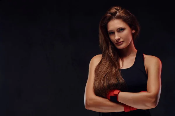一个美丽的运动女拳击手的肖像在运动服和包扎的手 摆出交叉双臂 在深色纹理背景下隔离 — 图库照片