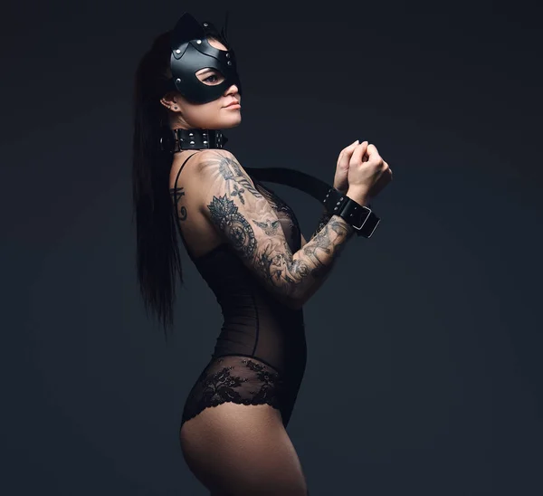 Σέξι γυναίκα που φοράει μαύρα εσώρουχα σε Bdsm γάτα δερμάτινη μάσκα και αξεσουάρ θέτοντας σε σκούρο φόντο. — Φωτογραφία Αρχείου