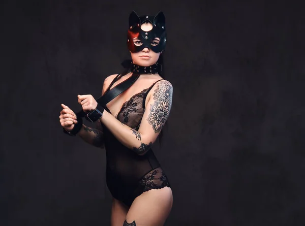 Sexy Frau trägt schwarze Dessous in bdsm Katzenledermaske und Accessoires posiert auf dunklem Hintergrund. — Stockfoto