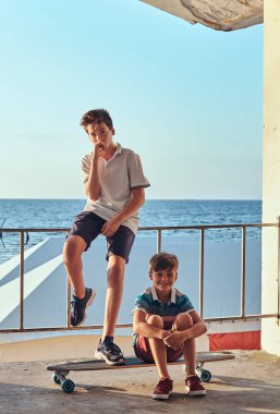 İki küçük bir sahil çerçevede Otokorkuluk yakın bir kaykay ile poz kardeşler.