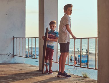 İki küçük sahil çerçevede Otokorkuluk yakın bir kaykay ile bir gün batımında ayakta kardeşler.