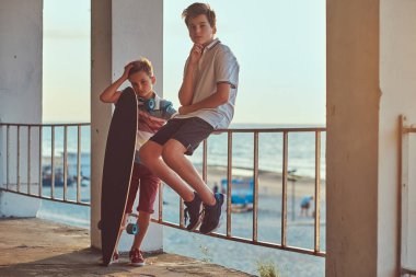 İki küçük sahil çerçevede Otokorkuluk yakın bir kaykay ile bir gün batımında ayakta kardeşler.