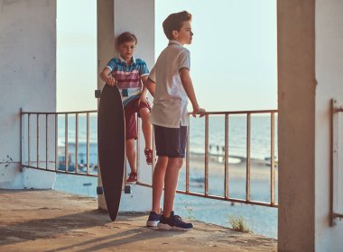 İki küçük sahil çerçevede Otokorkuluk yakın bir kaykay ile bir gün batımında ayakta kardeşler.