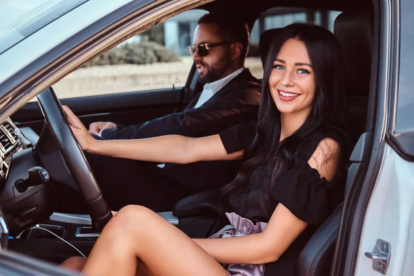 Hermosa pareja bien vestida sentada en los asientos delanteros en el coche de lujo . — Foto de Stock