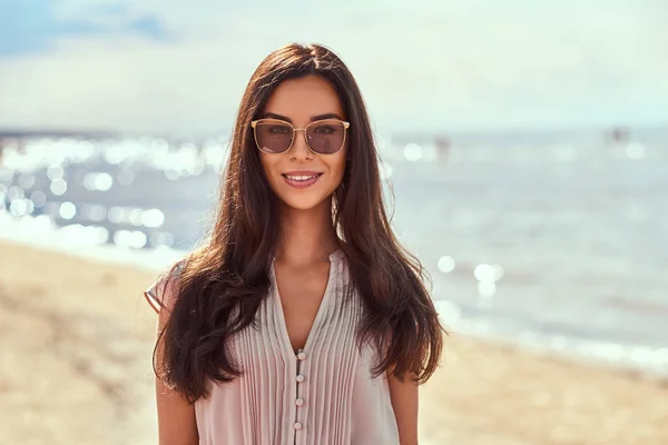 Portrait of a happy beautiful brunette girl with long hair in sunglasses and dress on the beach. — Stock Photo, Image