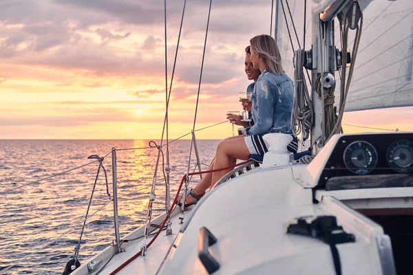 两个女朋友在游艇上放松 手里拿着酒杯 在公海上日落的时候 — 图库照片