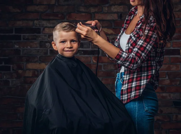 Söt förskolebarn pojke få frisyr. Barn Frisör med trimmer skär liten pojke i ett rum med loft interiör. — Stockfoto