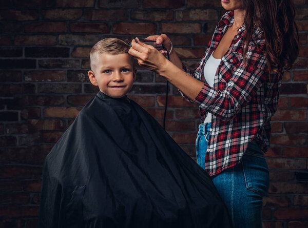 Cute preschooler boy getting haircut. Children hairdresser with trimmer is cutting little boy in the room with loft interior.