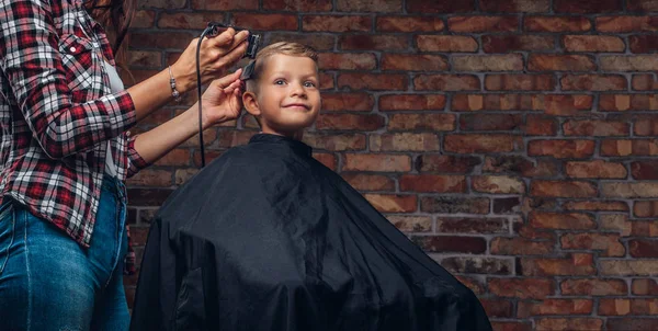 Милий хлопчик дошкільнята отримує зачіску. Дитячий перукар з тримером ріже маленького хлопчика в кімнаті з інтер'єром лофт . — стокове фото