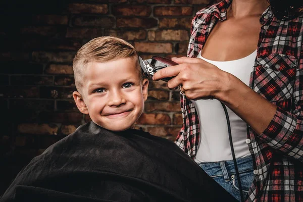 Söt förskolebarn pojke få frisyr. Barn Frisör med trimmer skär liten pojke i ett rum med loft interiör. — Stockfoto