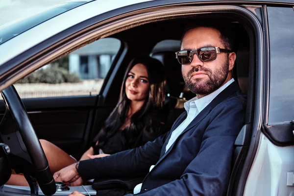 Hermosa pareja bien vestida sentada en los asientos delanteros en el coche de lujo . — Foto de Stock