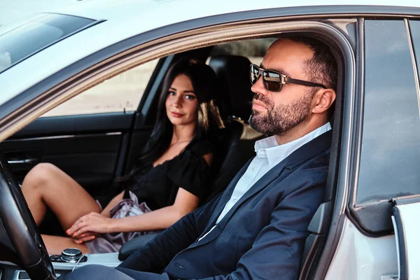 Hermosa pareja bien vestida sentada en los asientos delanteros en el coche de lujo . — Foto de Stock