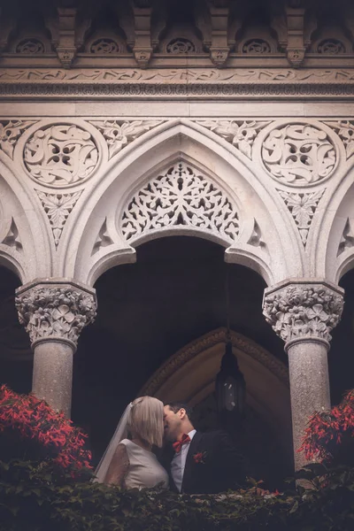 Preciosa pareja de recién casados - novia y novio beso mientras que de pie contra el viejo hermoso palacio de piedra al aire libre . —  Fotos de Stock