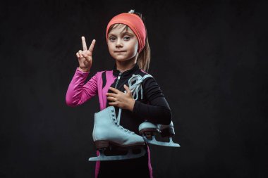 Spor içinde giyinmiş emin küçük patenci kız buz pateni tutar ve zafer el gösterir. Karanlık dokulu bir arka plan üzerinde izole.