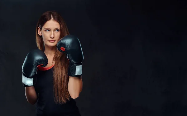 Mujer deportiva vestida con ropa deportiva con guantes de boxeo posando en un estudio. Aislado sobre un fondo de textura oscura . — Foto de Stock