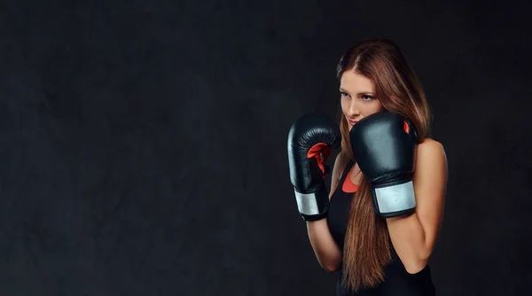 Femme sportive vêtue de vêtements de sport portant des gants de boxe posant dans un studio. Isolé sur un fond texturé foncé . — Photo