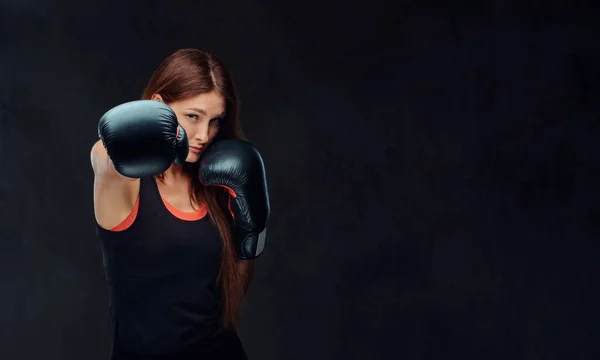 Mujer deportiva en ropa deportiva con un casco protector y guantes de boxeo, entrenamiento en el gimnasio. Aislado sobre fondo de textura oscura . —  Fotos de Stock