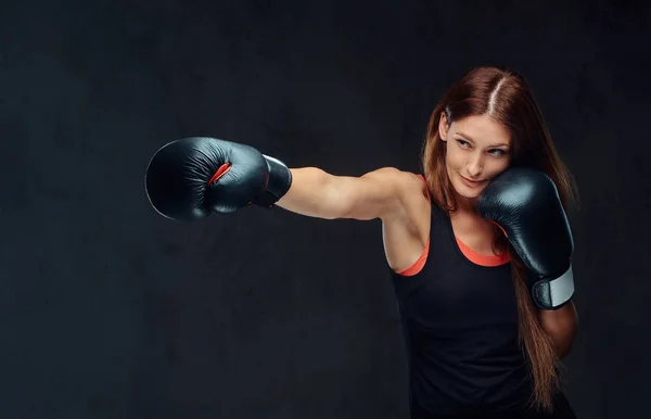 Mujer deportiva en ropa deportiva con un casco protector y guantes de boxeo, entrenamiento en el gimnasio. Aislado sobre fondo de textura oscura . — Foto de Stock