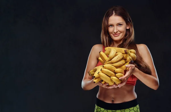 Mulher morena sorridente vestida com sutiã esportivo segura bananas. oncept de dieta saudável . — Fotografia de Stock