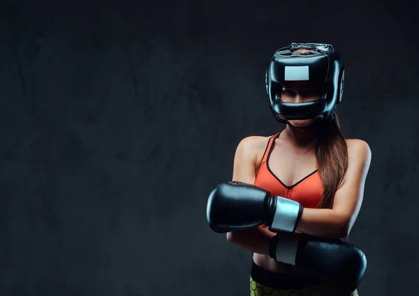 Femme sportive en soutien-gorge de sport portant un casque de protection et des gants de boxe, posant dans un studio. Isolé sur un fond texturé foncé . — Photo