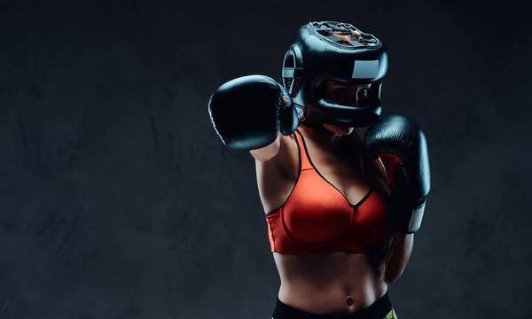 Mujer deportiva en sujetador deportivo con un casco protector y guantes de boxeo, entrenamiento en el gimnasio. Aislado sobre un fondo de textura oscura . —  Fotos de Stock