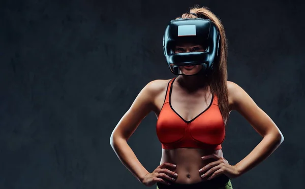 Sportive woman in sports bra wearing a protective helmet, posing in a studio. Isolated on dark textured background. — Stock Photo, Image