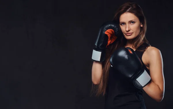 Porträt einer sportlichen Frau in Sportbekleidung mit Boxhandschuhen, die in einem Studio posiert. isoliert auf dunklem, strukturiertem Hintergrund. — Stockfoto