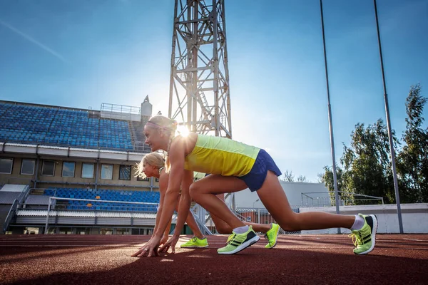 Dos atletas velocistas preparándose para comenzar una carrera en una pista roja en el estadio de atletismo . — Foto de Stock