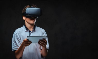 Genç öğrenci çocuk portresi sanal gerçeklik gözlükleri ve tablet bilgisayar kullanarak bir beyaz gömlek giymiş.